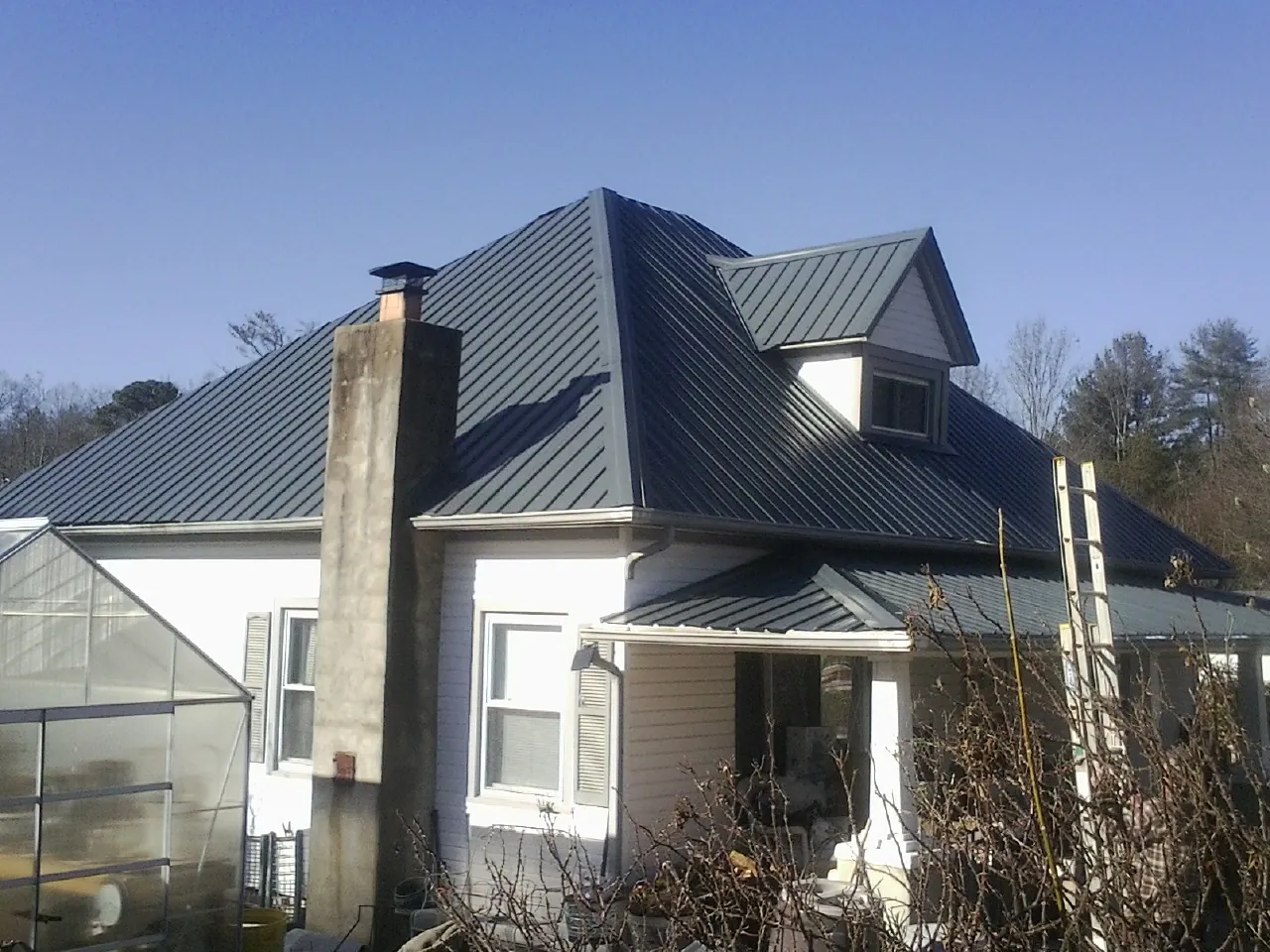 Dark blue standing seam metal roof on a white farmhouse with dormer — Slate & Tile Roof Repair by Roofing Brothers in Ekron