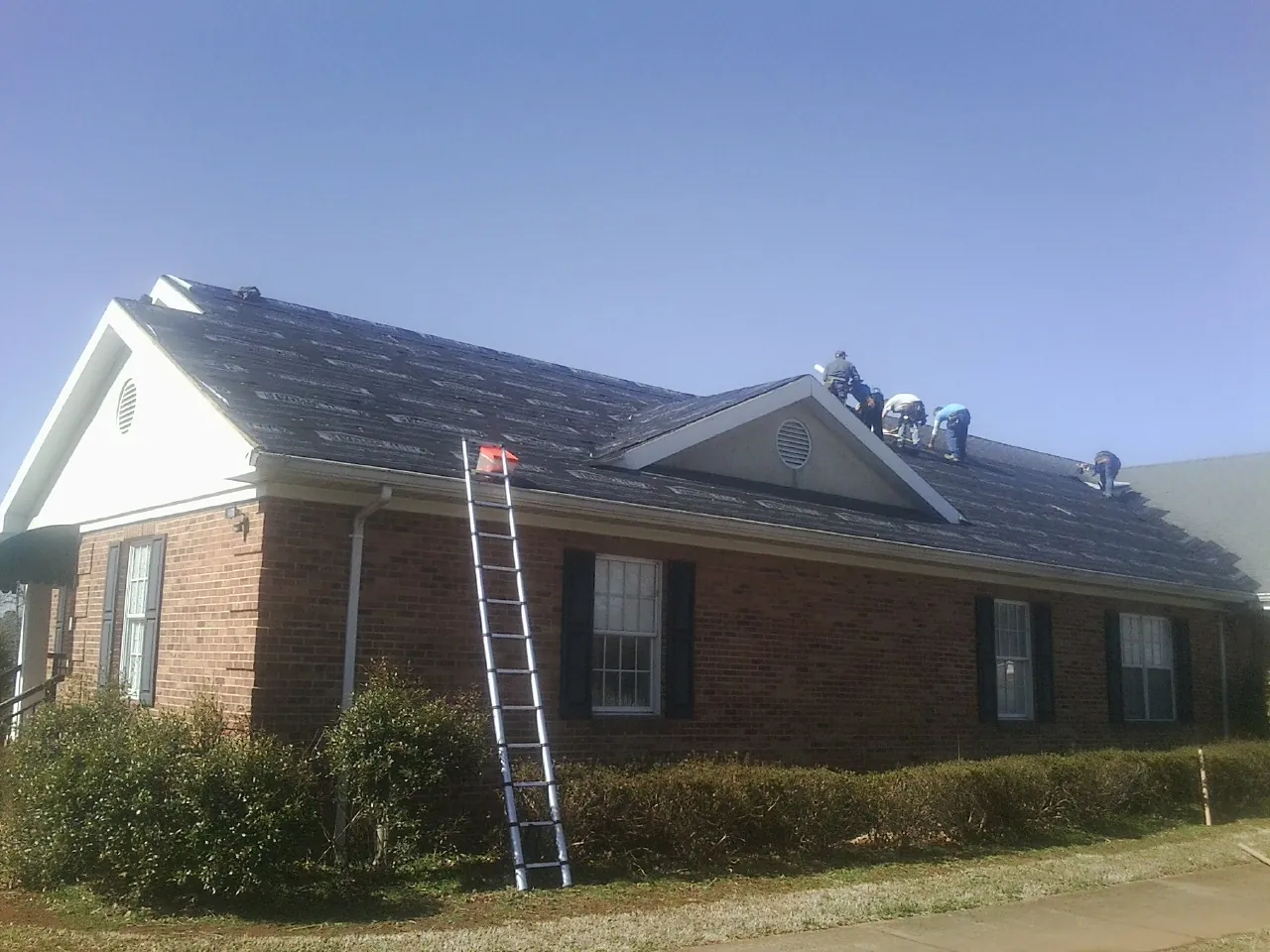 Crew tearing shingles off a brick ranch roof with a ladder set — Emergency Roof Repair work by our crew in Ekron