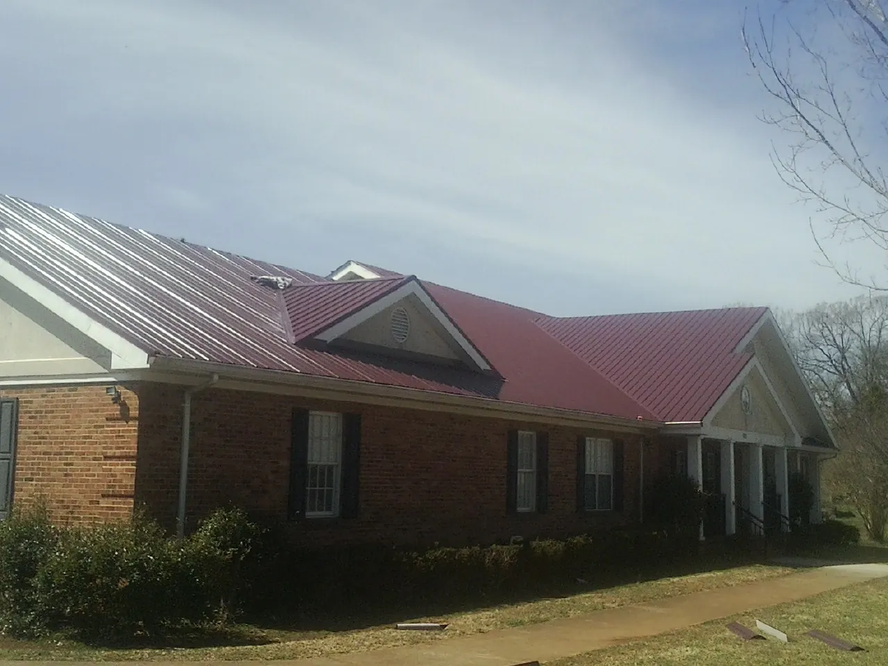 Red metal roof with gabled entries on a long brick building, from a Hail Damage Roof Repair job in Ekron