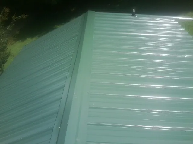 New green metal panels meeting at the ridge of a roof — Flat Roof Repair work by our crew in Ekron