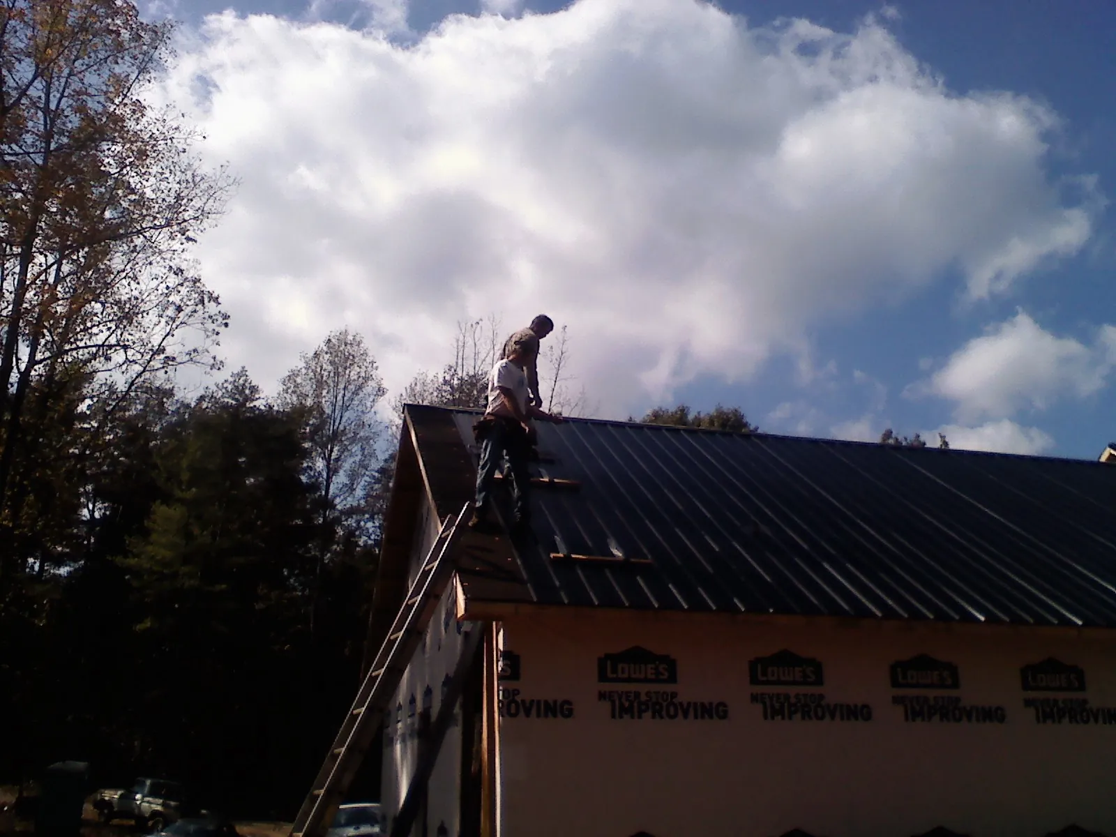 Roofer fastening dark metal panels high against a cloudy sky, from a Roof Inspection job in Ekron