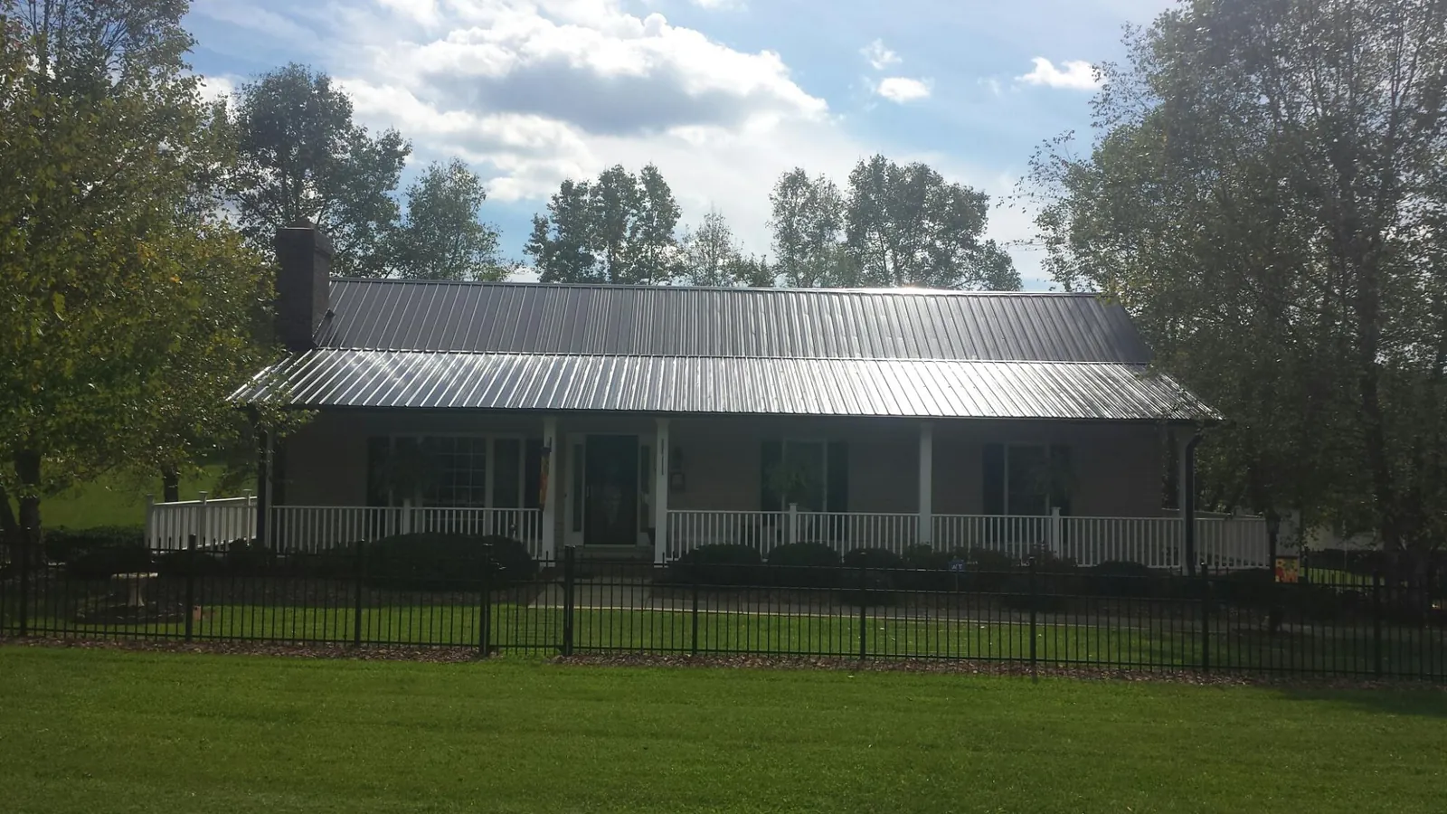 Gray metal roof on a brick ranch with a full width front porch — Gutter Guard Installation work by our crew in Ekron